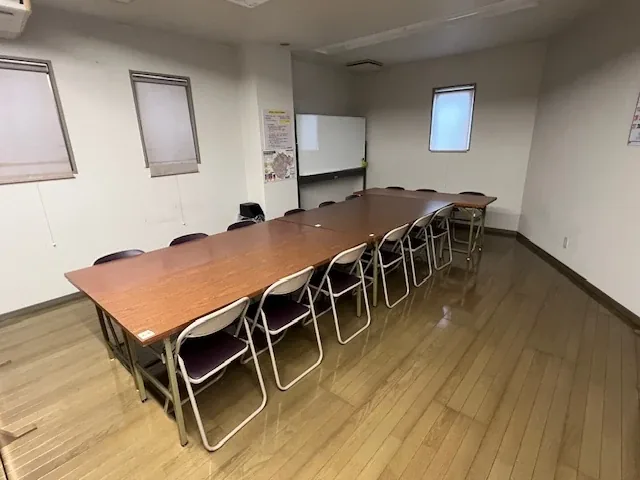 会議室。長机を囲んで椅子が並び、奥にホワイトボードがあります。